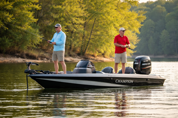 Two men fishing on a motorboat near a wooded lakeshore.