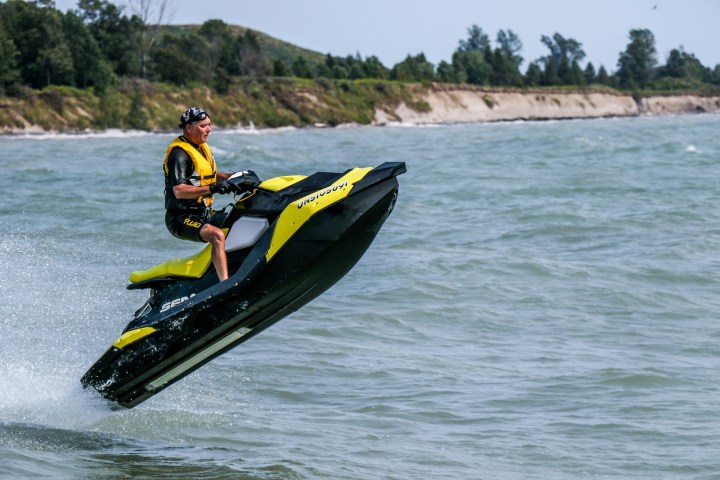 Person riding a yellow jet ski jumping over waves near a shoreline.
