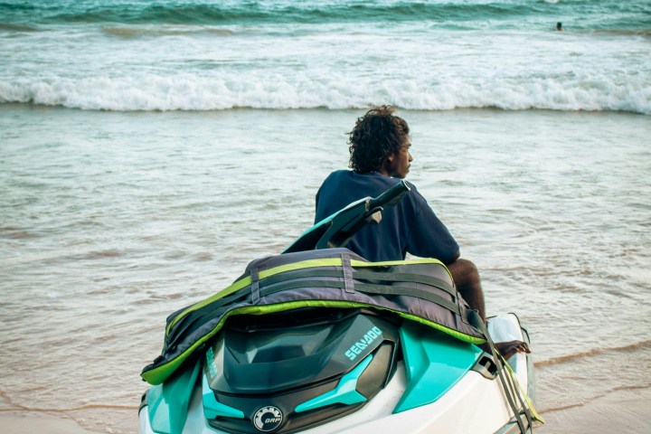 Person sitting on a jet ski by the shore with waves in the background.