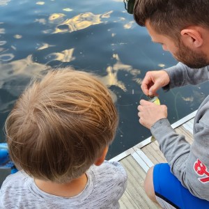 Man and child on dock fishing, man handling bait near water.