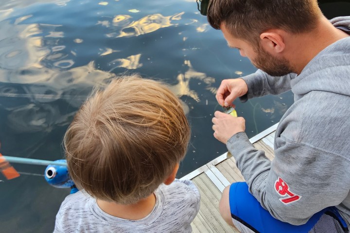 Man and child on dock fishing, man handling bait near water.