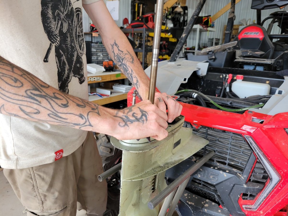 Person with tattoos working on a green machine part near a red vehicle in a garage.