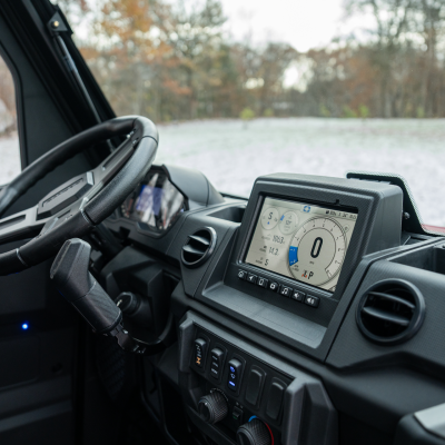 Interior of a vehicle showing a steering wheel and digital dashboard against an outdoor background.