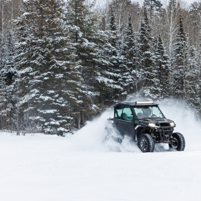 ATV driving through snow in a forest with snow-covered trees in the background.