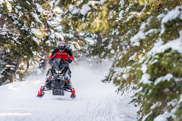 Person riding a snowmobile on a snowy trail surrounded by trees.