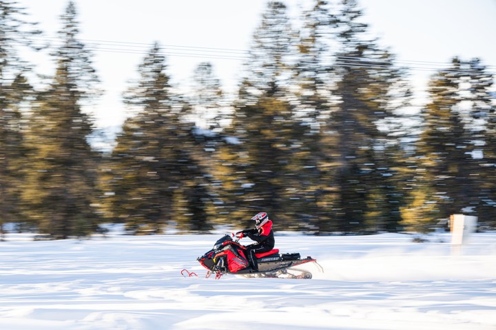 Person riding a red snowmobile on a snowy path with blurred trees in the background.