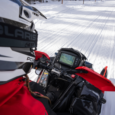 Person riding a snowmobile on a snowy trail, wearing a helmet and red jacket.