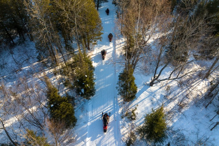 Aerial view of people riding snowmobiles on a snowy forest trail.