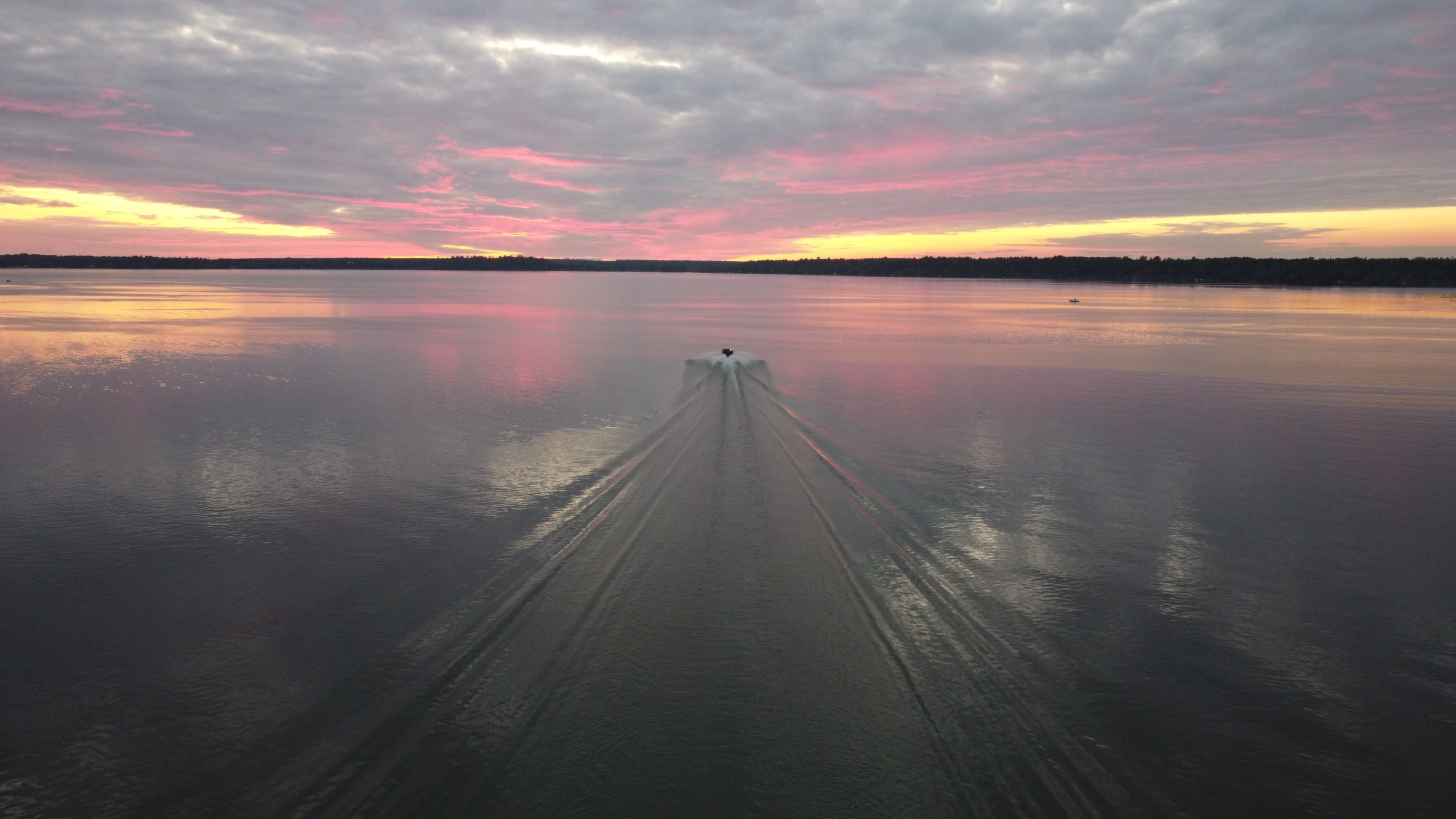 Boat moving on calm lake at sunset with pink clouds.